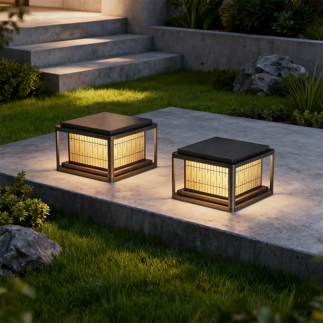 Pair of outdoor pillar LED lights brightening garden pathway with decorative lattice creating pattern at night.