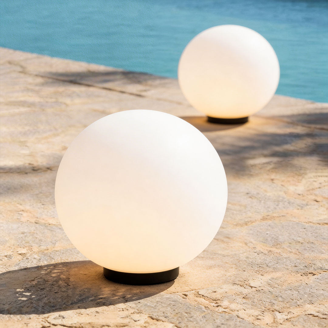 Pair of round landscape lighting globes on a stone pool deck with blue water in background!!