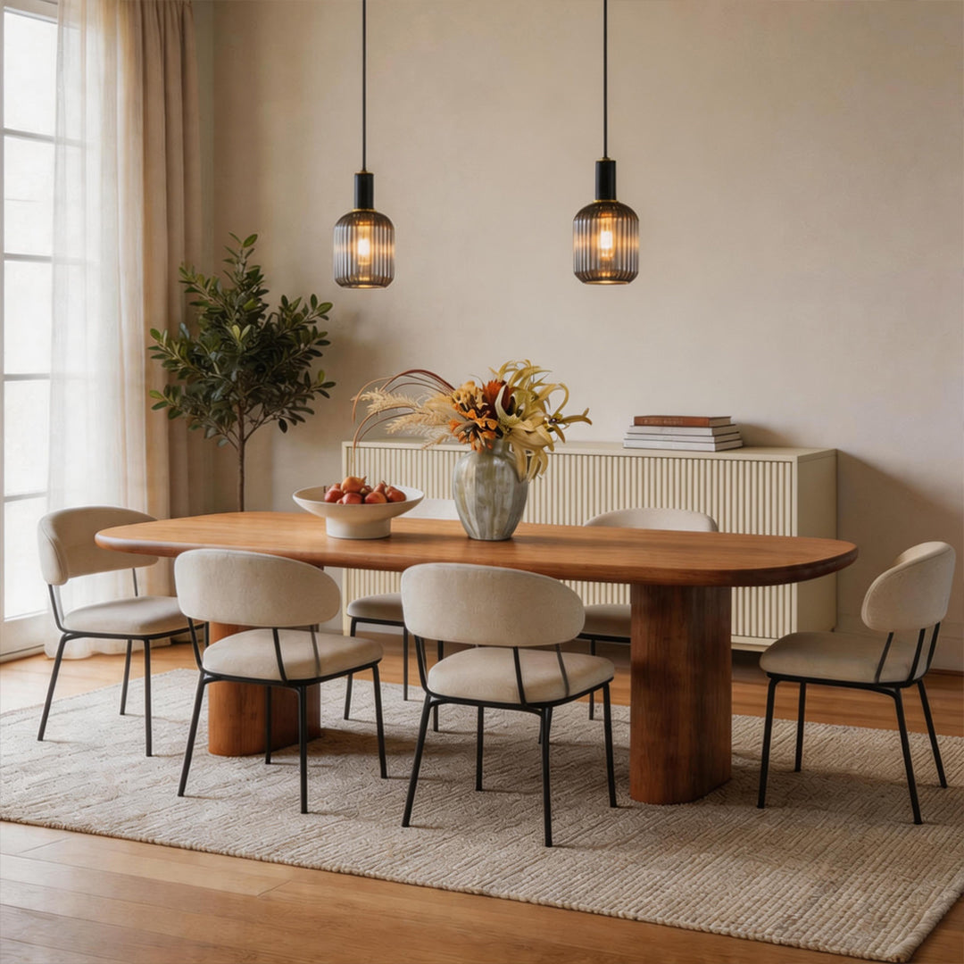 Pair of vintage glass pendant light fixtures glowing over a modern oval wood dining table set.