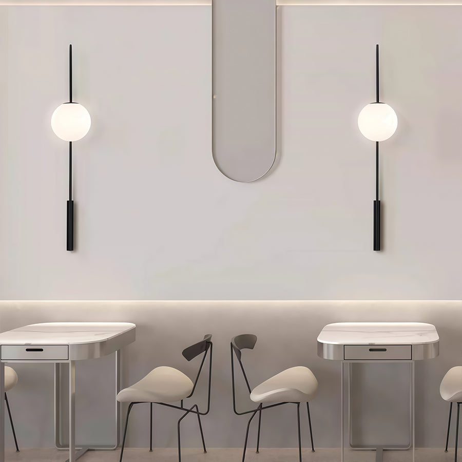Pair of wall arm lights with white cylindrical shades and black suspension rods in minimalist dining space.