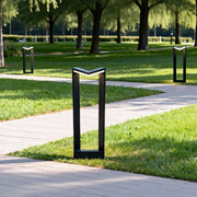 Square bollard light used along a park pathway creating structured and uniform outdoor lighting.