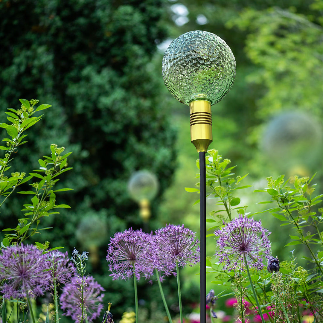 Pastel-toned crackle-glass globe glowing softly in a floral setting for decorative path landscape lighting.