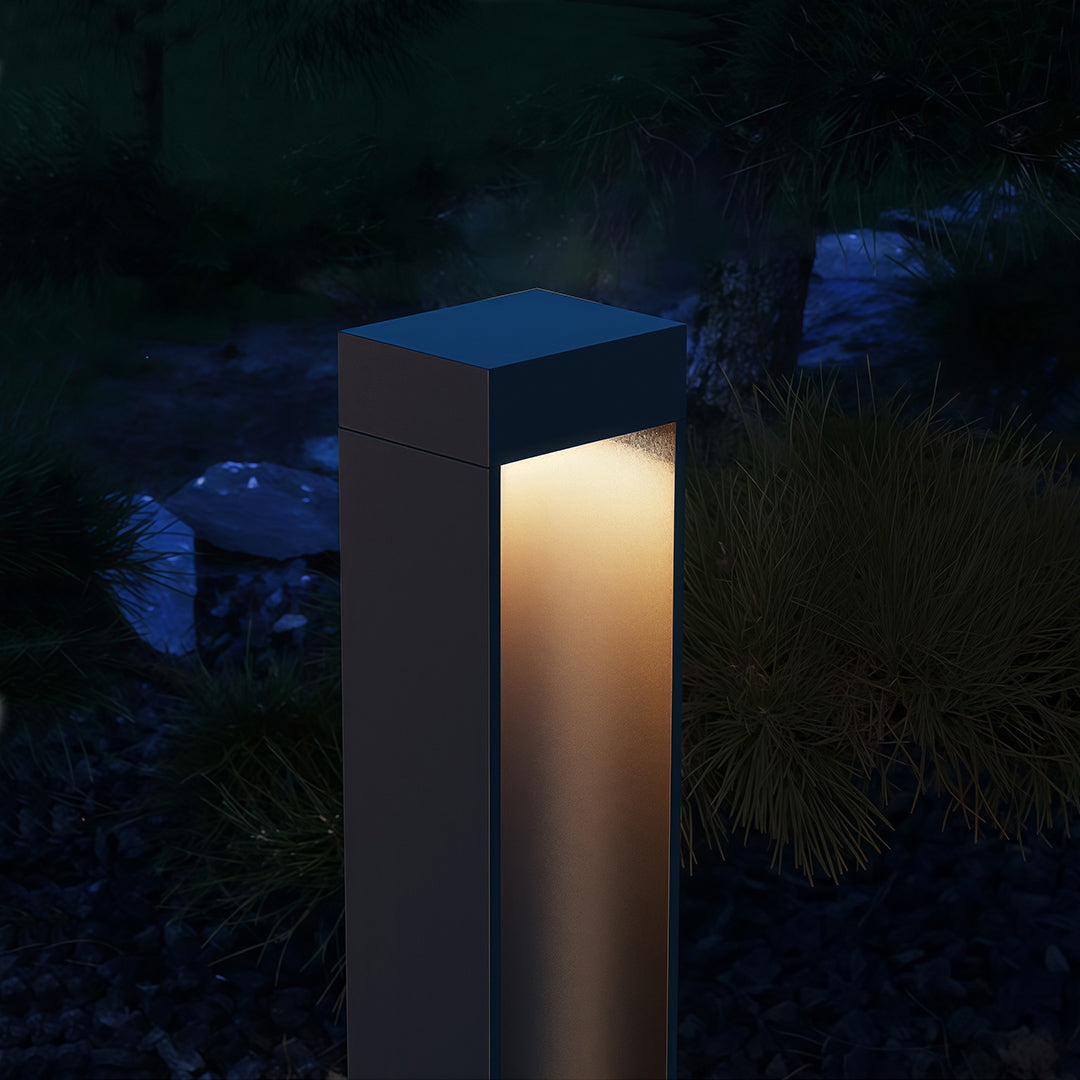 Path light stake in a garden with plants, adding a contemporary touch to the outdoor space.