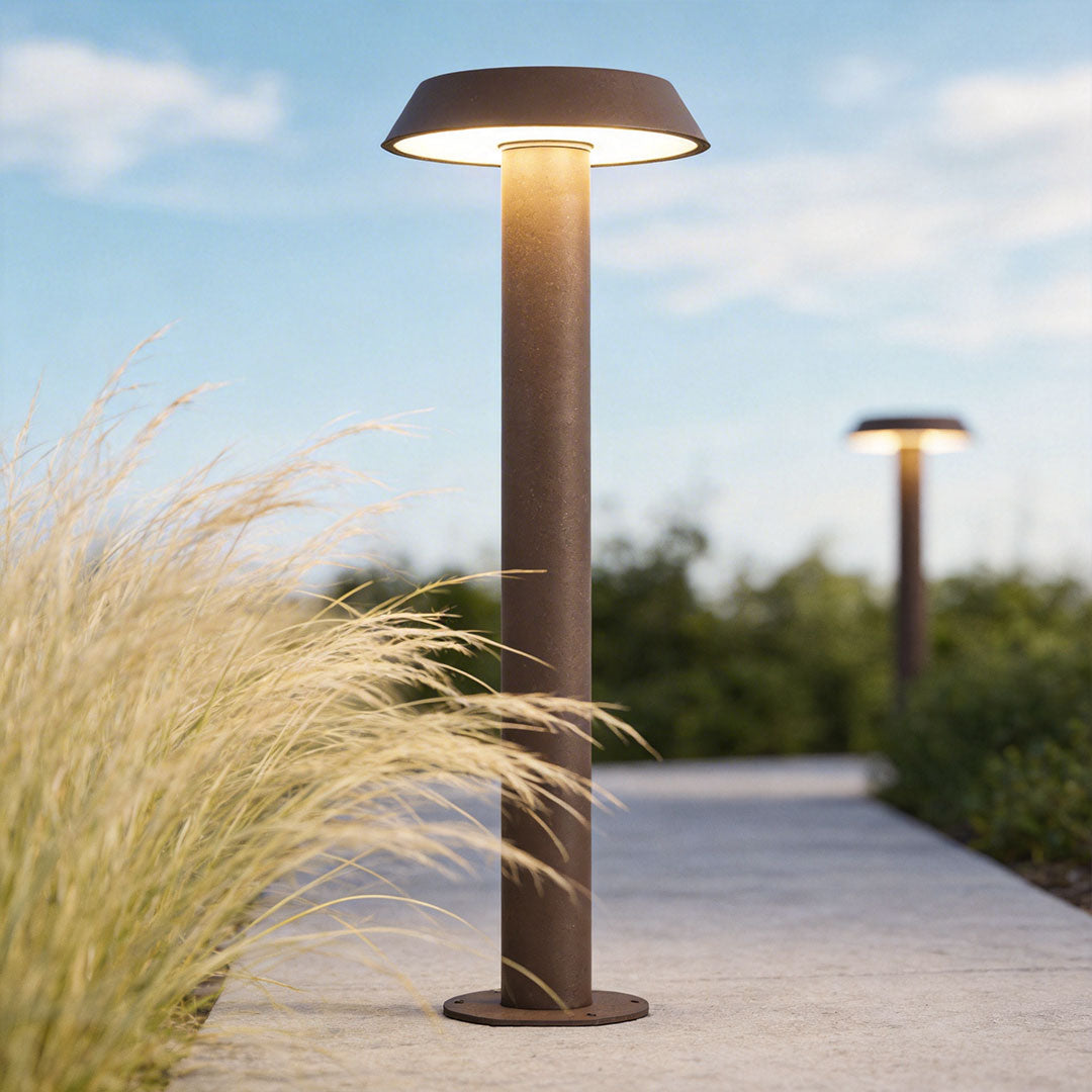 Path lighting LED beside a garden path, showing a modern outdoor bollard light with a wide flat shade and warm glow.