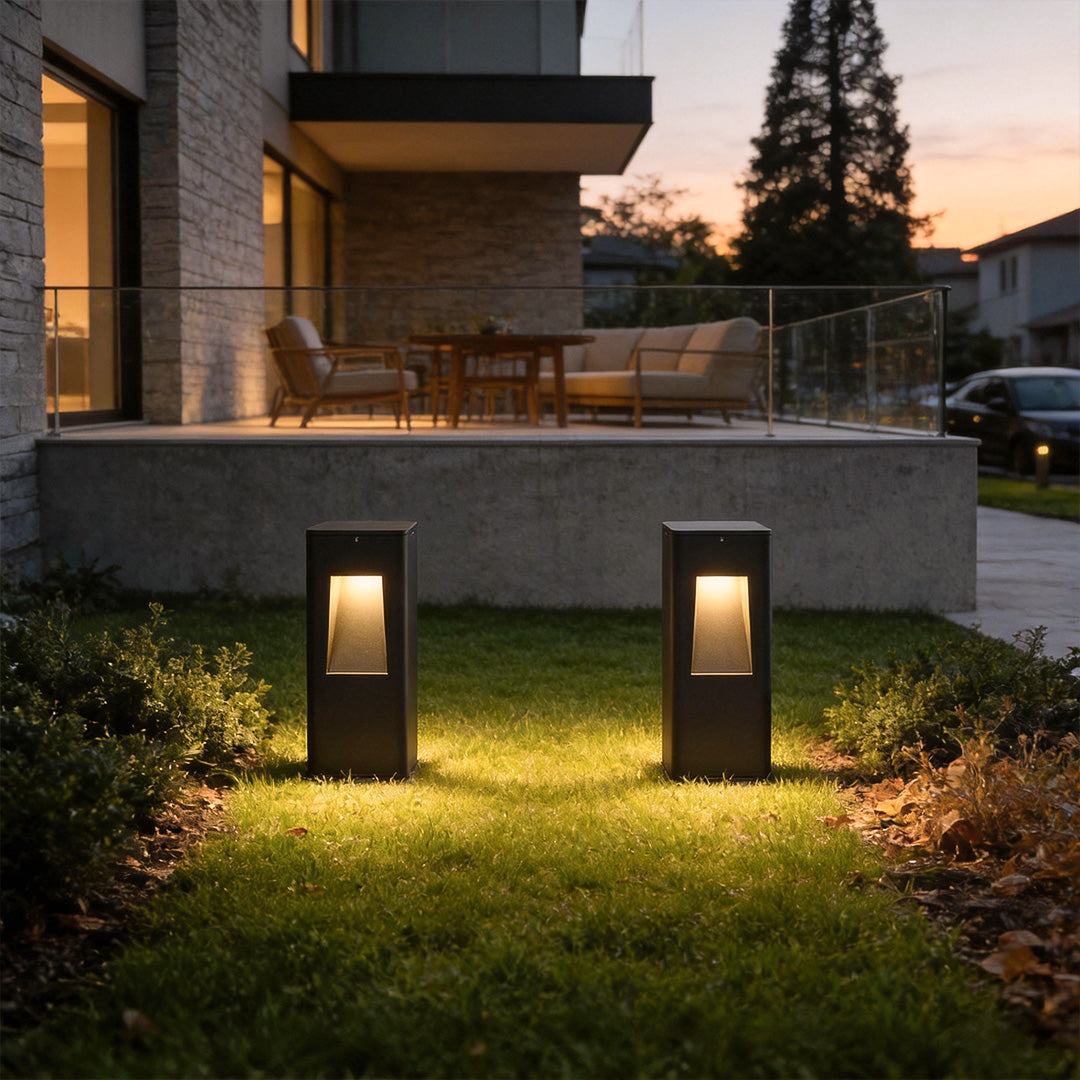 Pathway bollard lights illuminating a modern garden walkway beside a residential building at dusk.