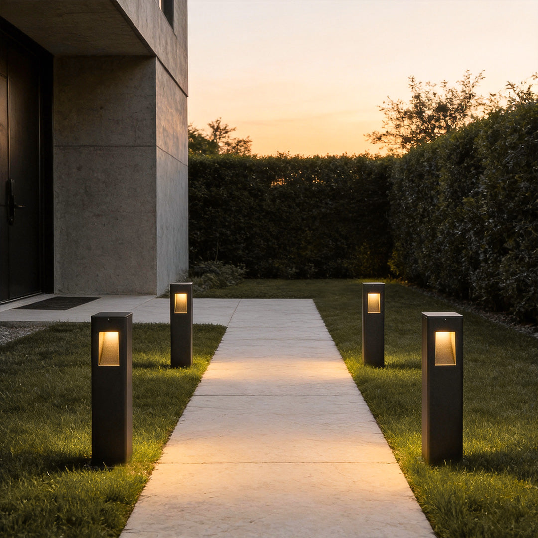 Pathway bollard lights providing soft illumination along a concrete pathway in a landscaped garden.