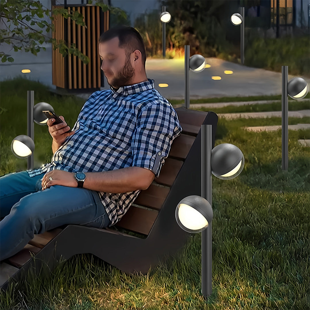 Pathway landscape lighting along lawn border with person adjusting fixture demonstrating versatile positioning capability