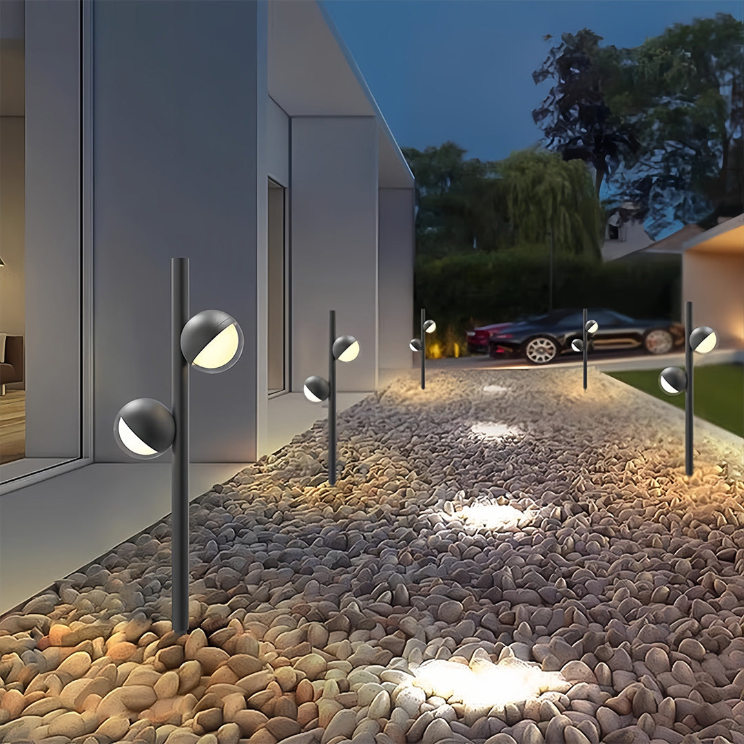 Pathway landscape lighting installation in residential garden with multiple fixtures along gravel path at dusk