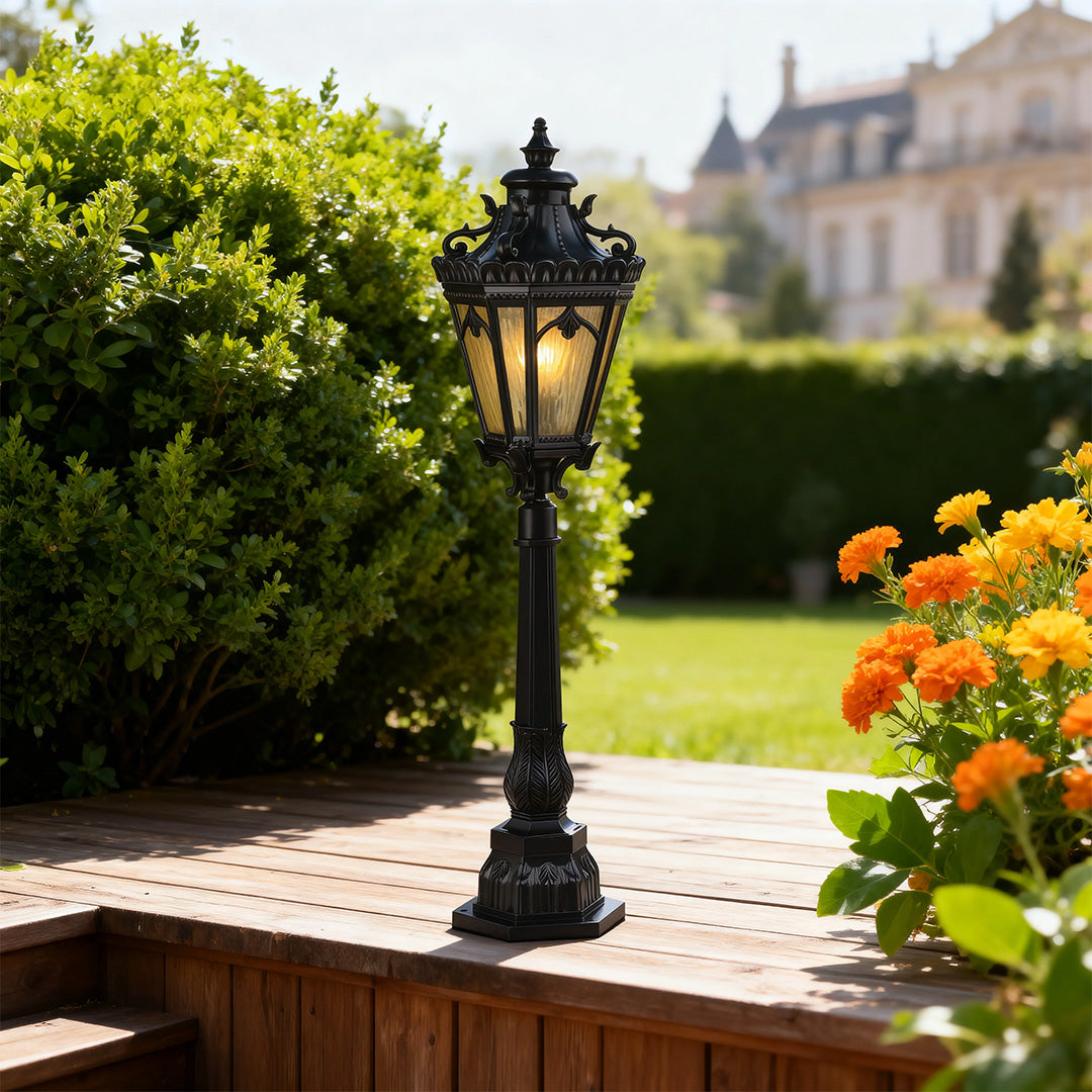 Pathway lighting bollard with ornate Victorian design standing on manicured lawn beside orange flowers and garden