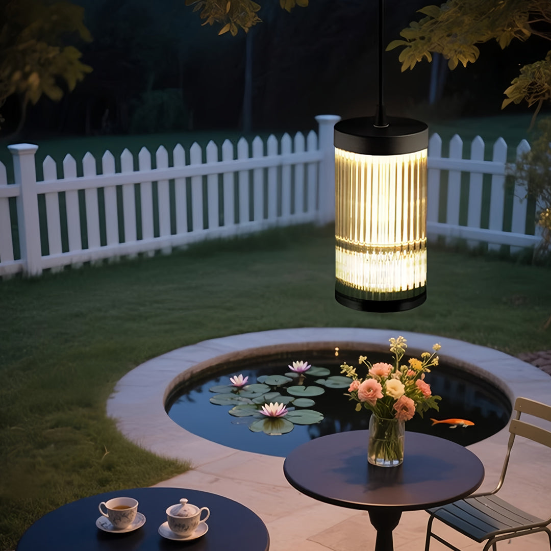 Elegant outdoor pendant light fixture hanging above a patio dining setup with ambient evening lighting.