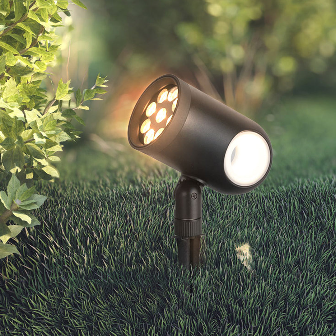 Outdoor waterproof spotlight casting patterned warm light onto trimmed landscape bushes.