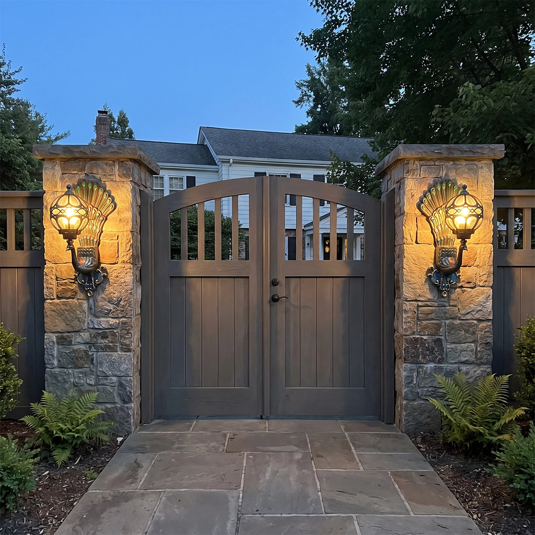 Peacock wall light fixtures mounted on stone gate pillars, adding warm decorative lighting to an outdoor entryway.
