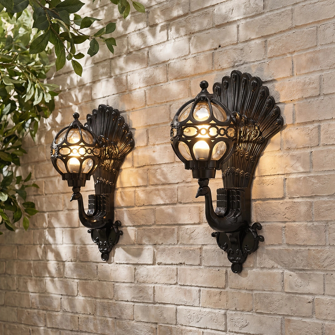 Pair of peacock wall light sconces with decorative shell-style backplates and warm glowing glass shades on a light brick wall.