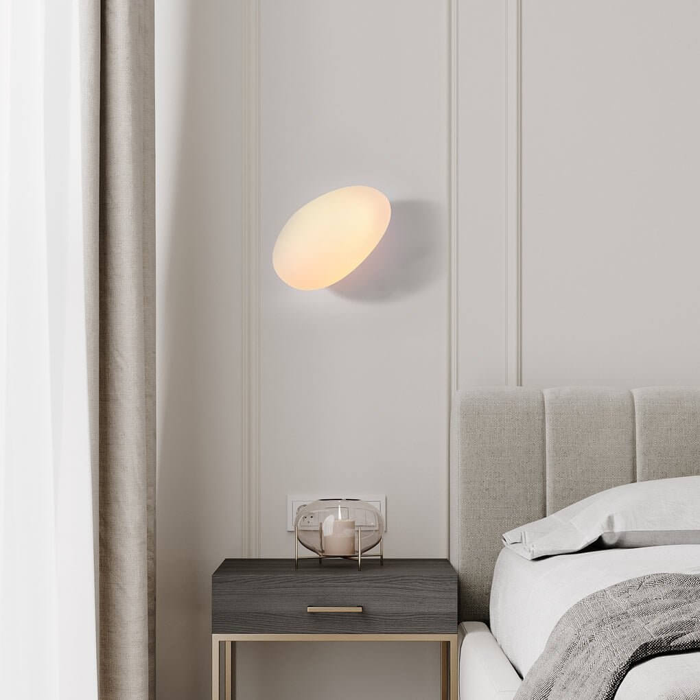 Pebbles wall lamp illuminating a minimalist bedside table with a warm and inviting light.