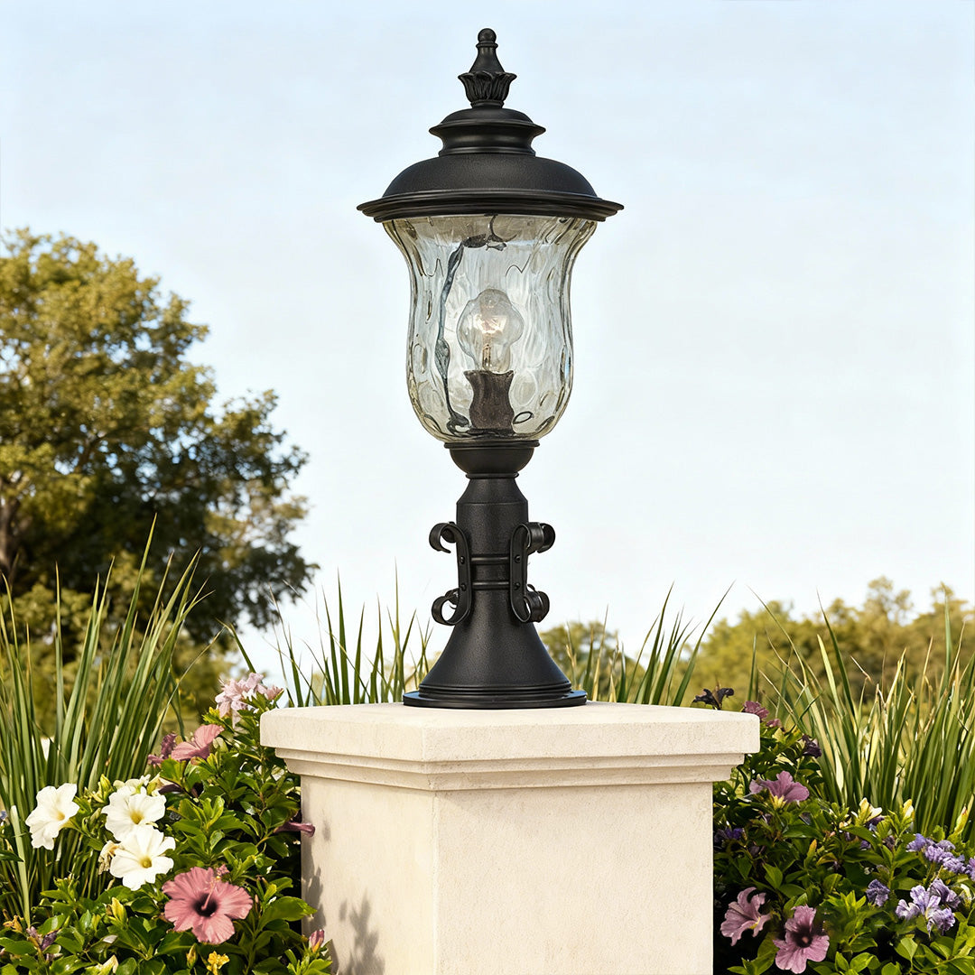 Pillar gate light mounted on white stone column in landscaped garden with pink flowers and trees