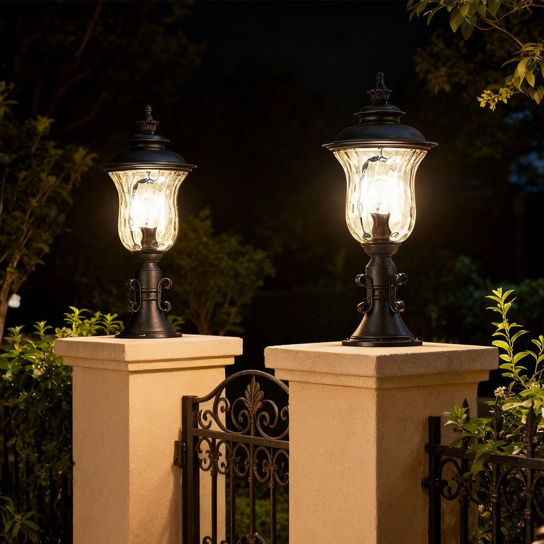 Pair of pillar gate lights glowing warmly on cream-colored entrance posts at dusk