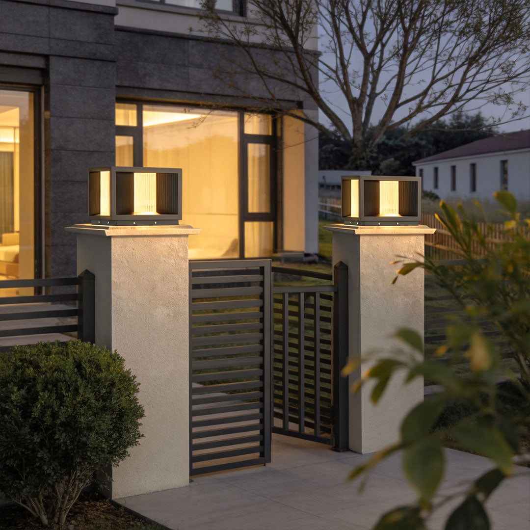 Pillar lighting with a black frame installed on stone pillars near a modern fence at night.