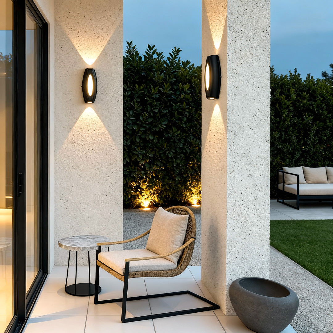 Warm glowing outside up down wall lights installed on tall exterior pillars, illuminating an outdoor seating area.