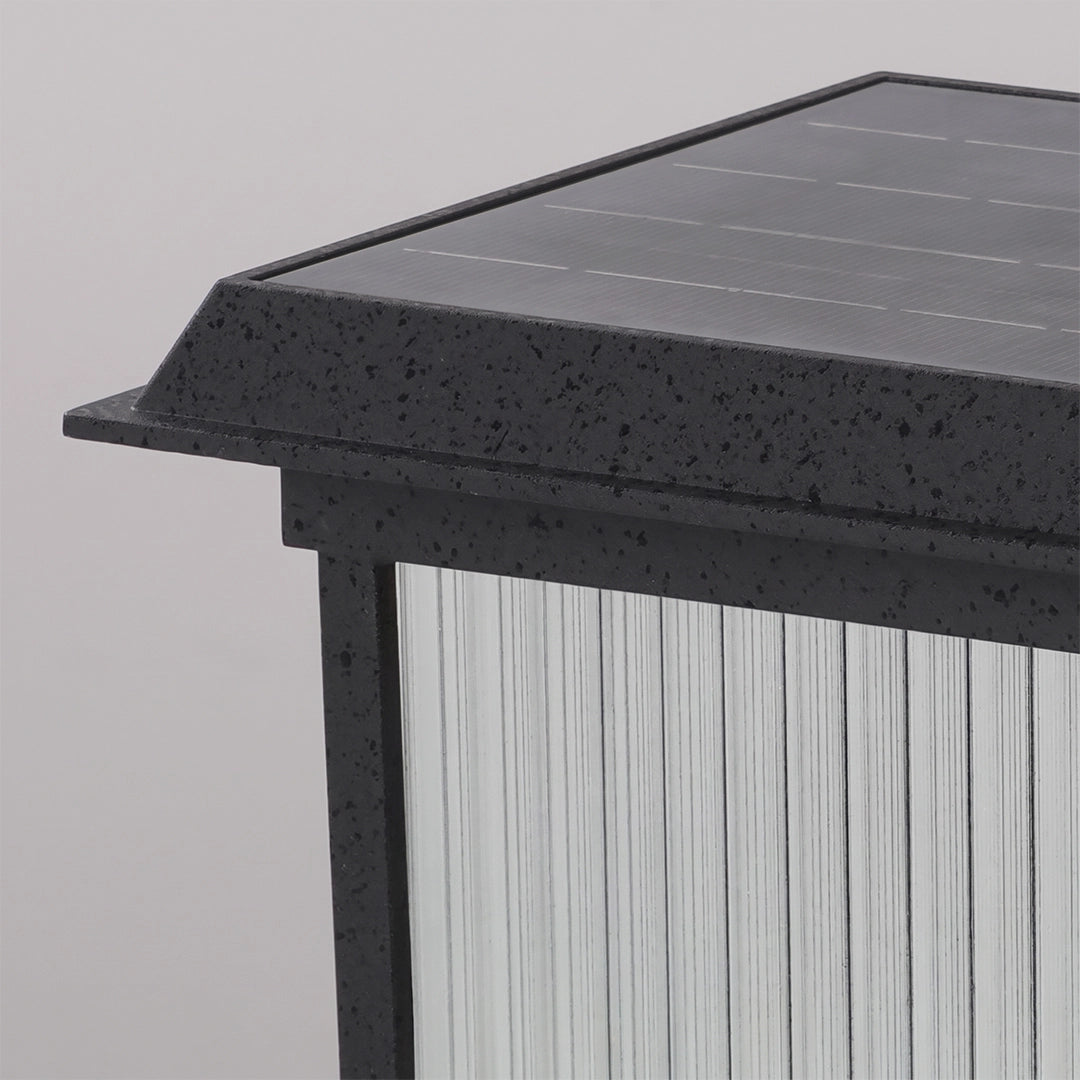 Close-up of a pillar solar light with a black speckled top, integrated solar panel, and clear ribbed side panels.