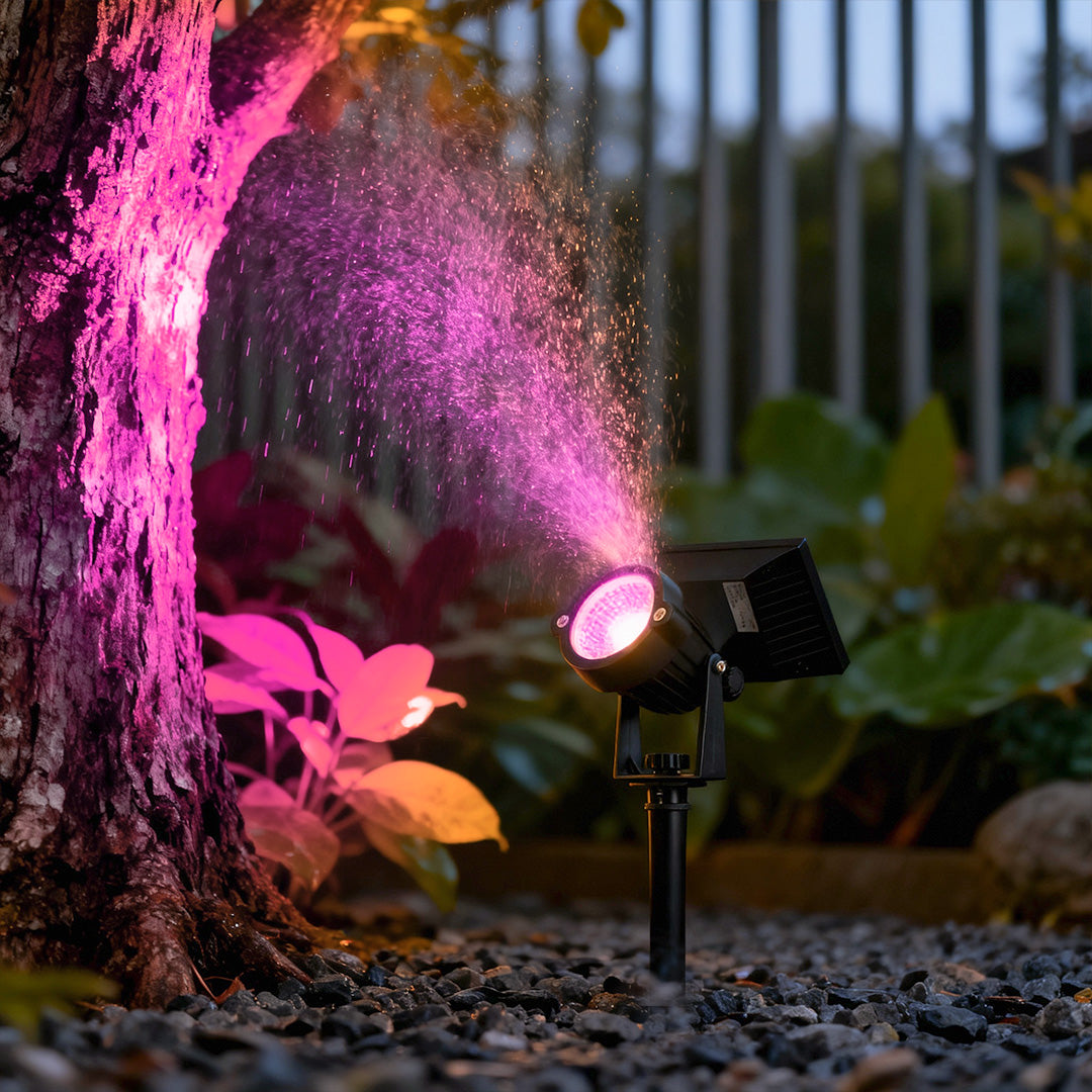 Ground spike solar lights casting pink accent light onto a tree trunk for decorative garden lighting.