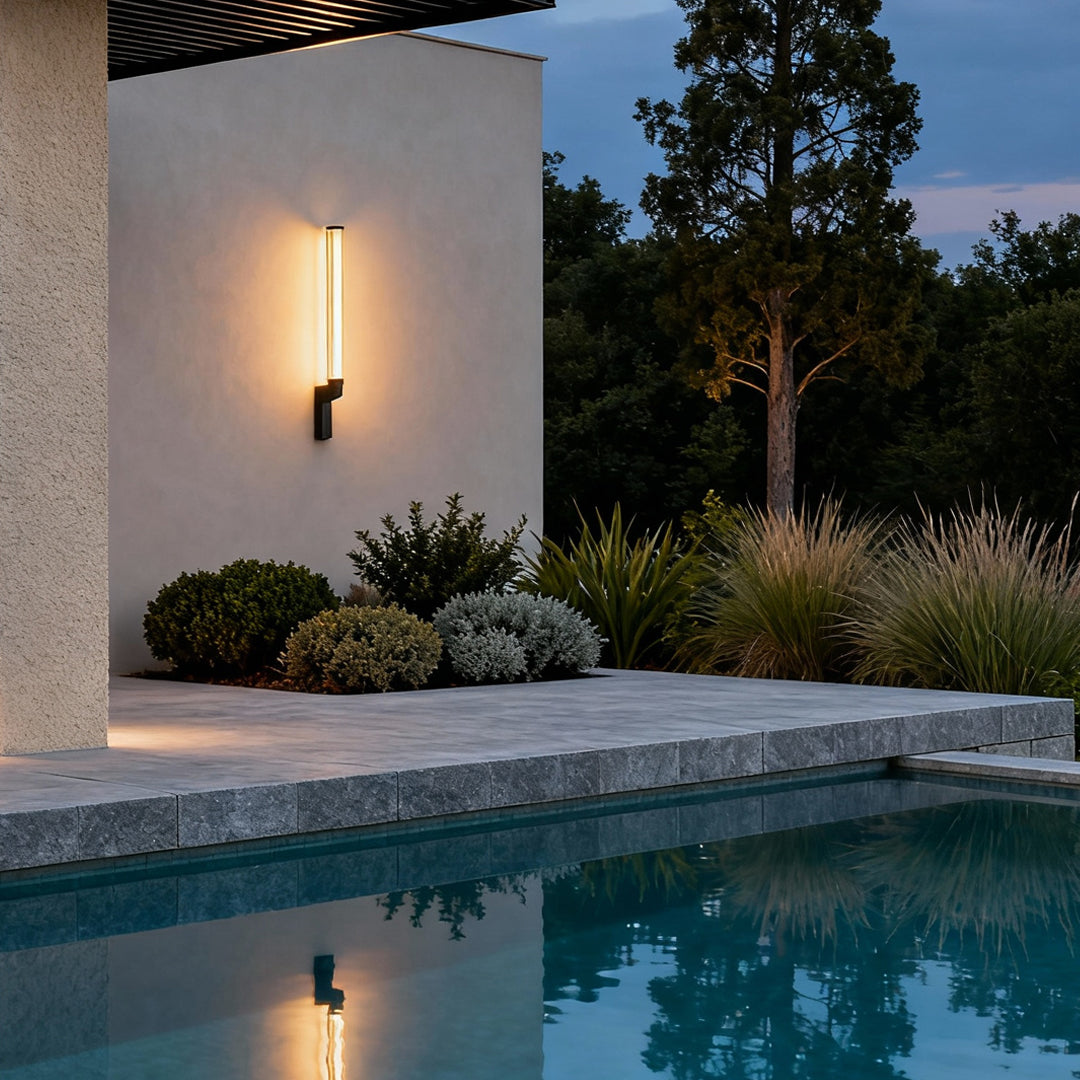 Warm glowing vertical outdoor sconces modern illuminating a white exterior wall by a poolside.