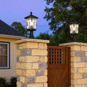 Pair of porch pillar lights glowing on stone columns flanking wooden gate entrance at twilight