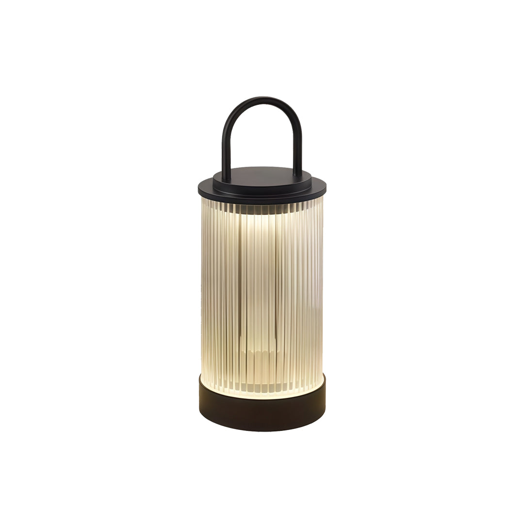 Small gold-toned portable lantern with ribbed diffuser emitting warm light on plain backdrop.