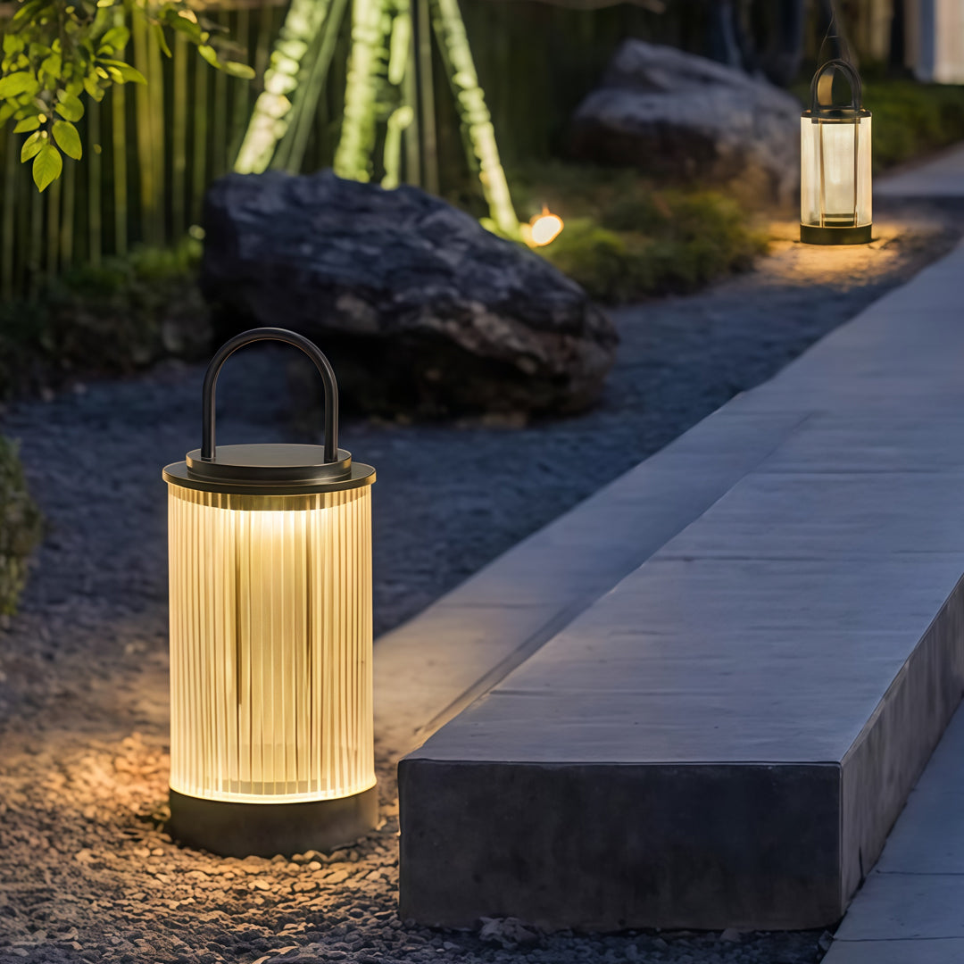 Modern portable lantern placed along exterior stone walkway providing gentle landscape illumination.