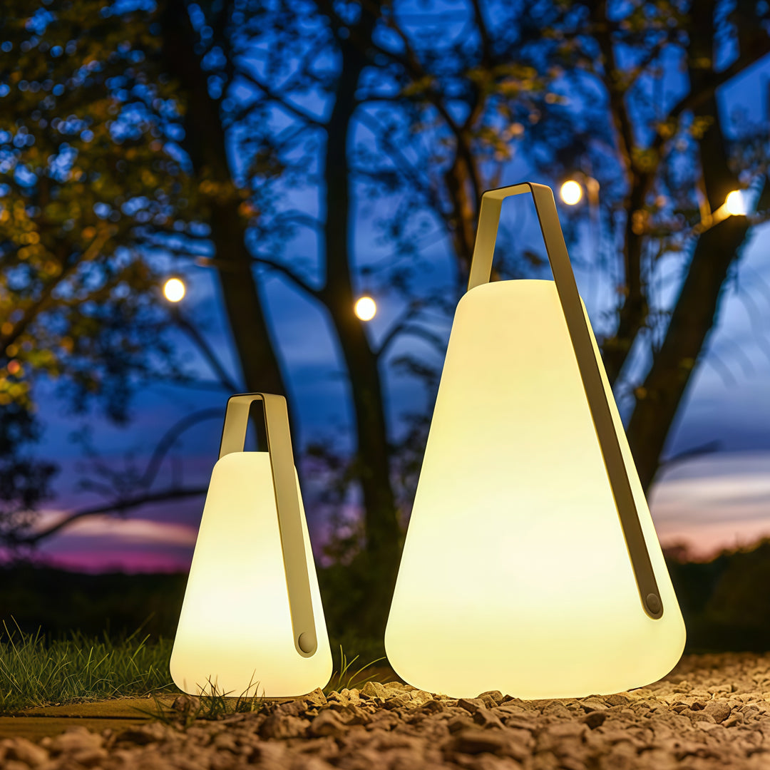 Three glowing portable led lanterns placed on grass during evening time, creating warm and inviting outdoor illumination.