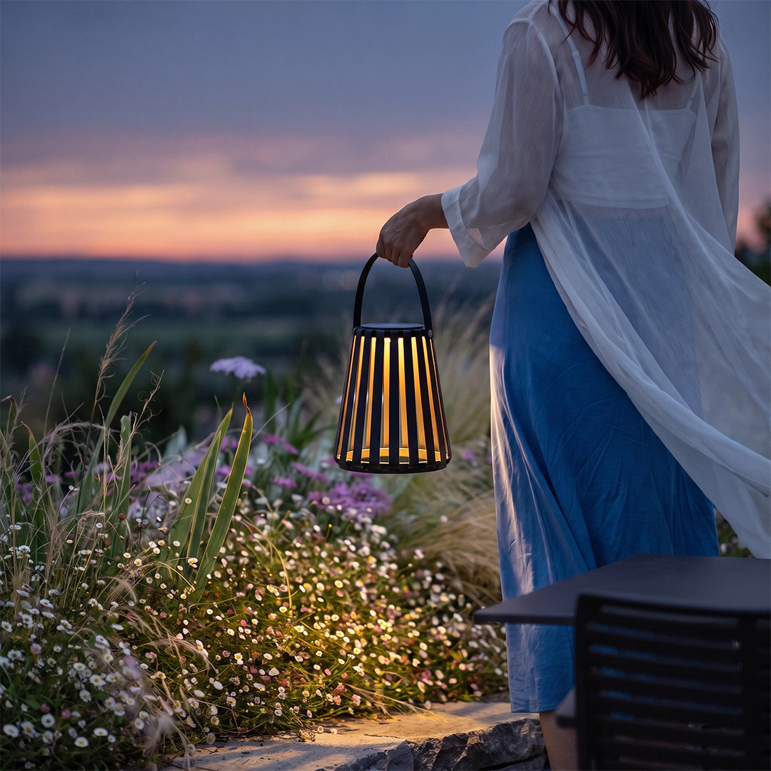 Portable LED light lantern carried by hand outdoors at sunset with warm light glowing through the slats.