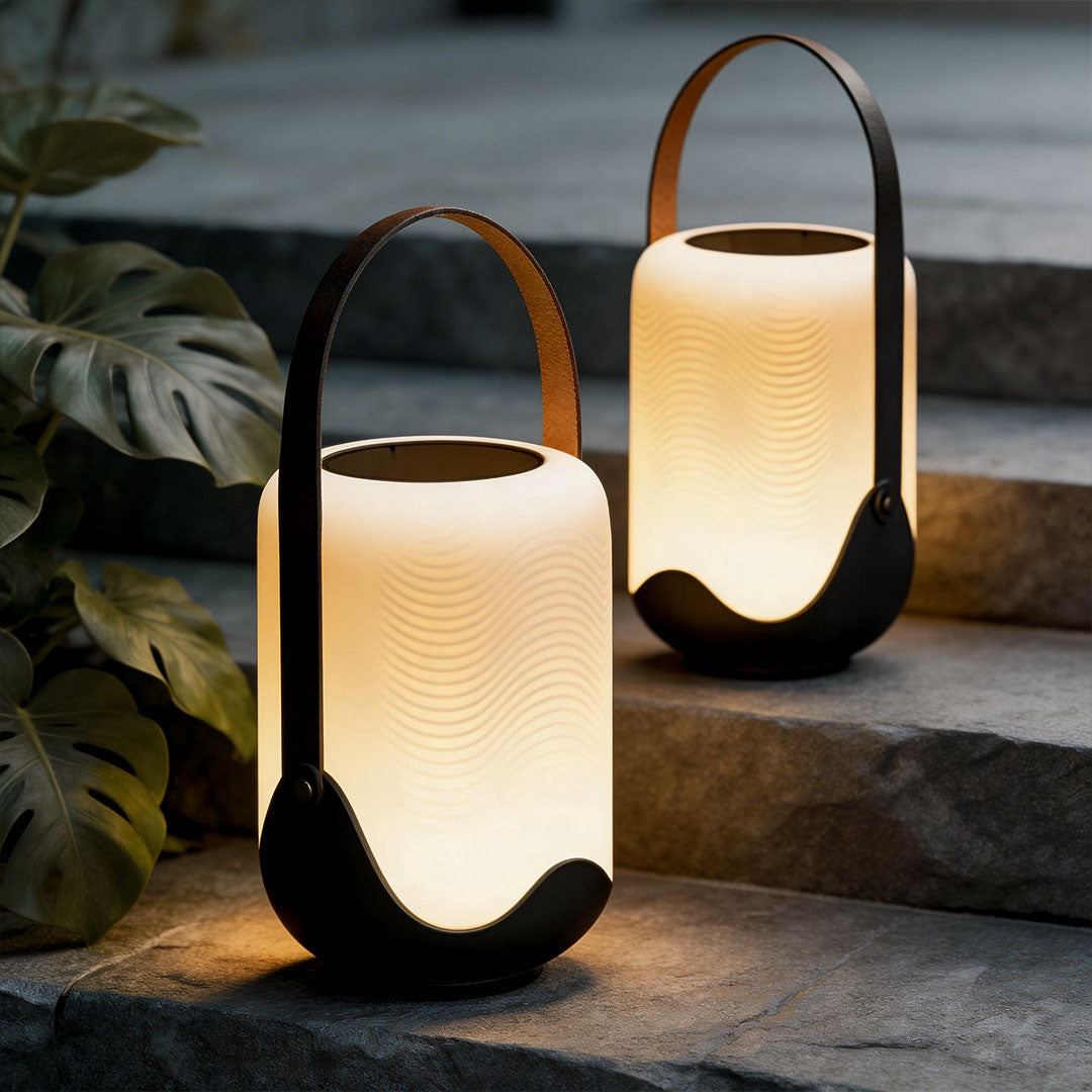 Portable solar lanterns with a modern design, placed on a wooden deck beside plants.
