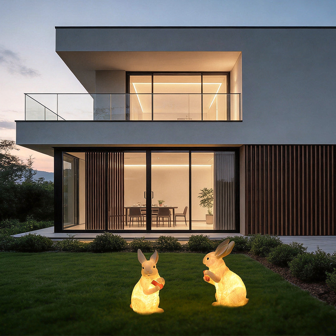 Pair of adorable rabbit garden lights glowing softly in front of a contemporary home at dusk.