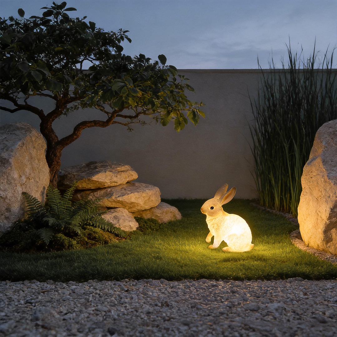 Charming rabbit garden light illuminating a pathway beside a modern house with warm yellow glow.