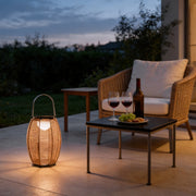 Rattan floor lantern illuminating a cozy outdoor seating area with warm ambient glow.