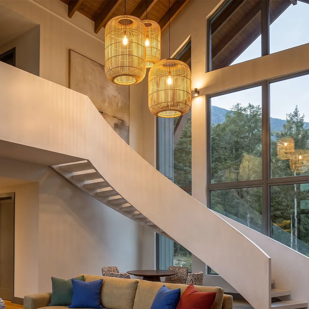 Rattan light pendants suspended in a high-ceiling living space beside a staircase and tall windows.