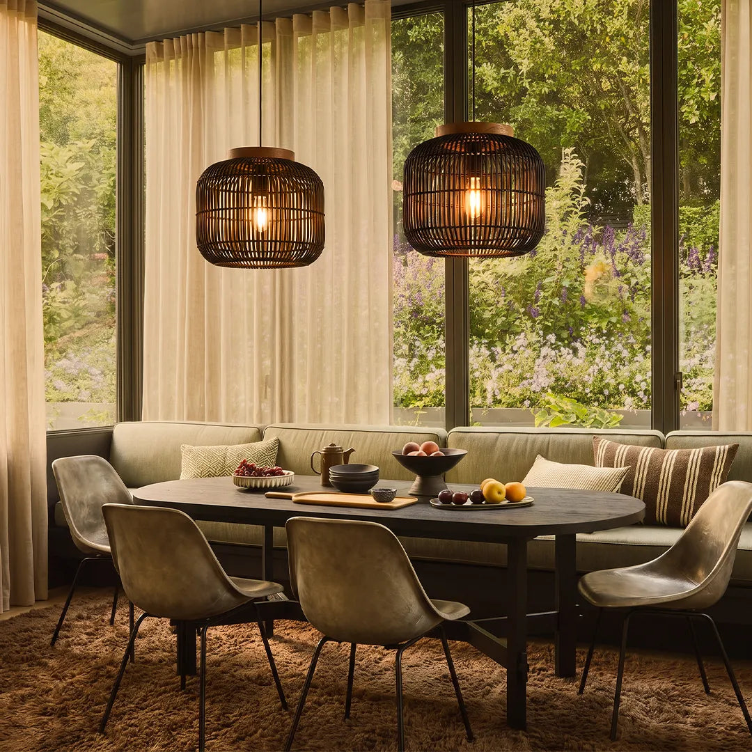 Rattan light pendants hanging above a dining table in a warm modern dining room with large windows.