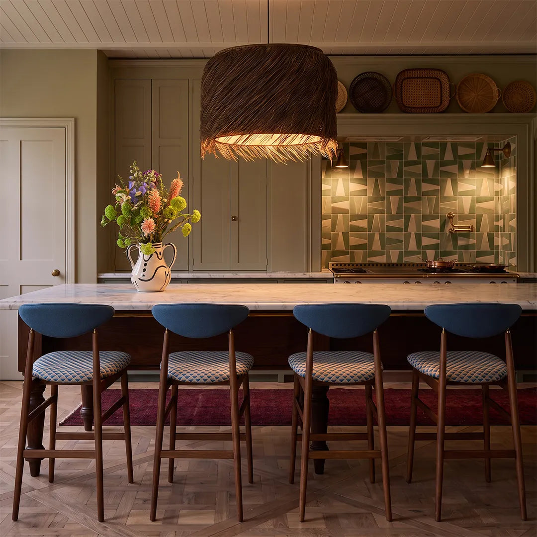 Rattan lighting pendants suspended above a kitchen island with blue bar stools and warm ambient lighting.