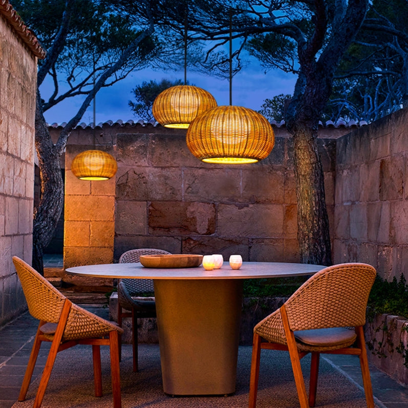 Rattan outdoor pendant light with a natural finish, hanging above a garden table.
