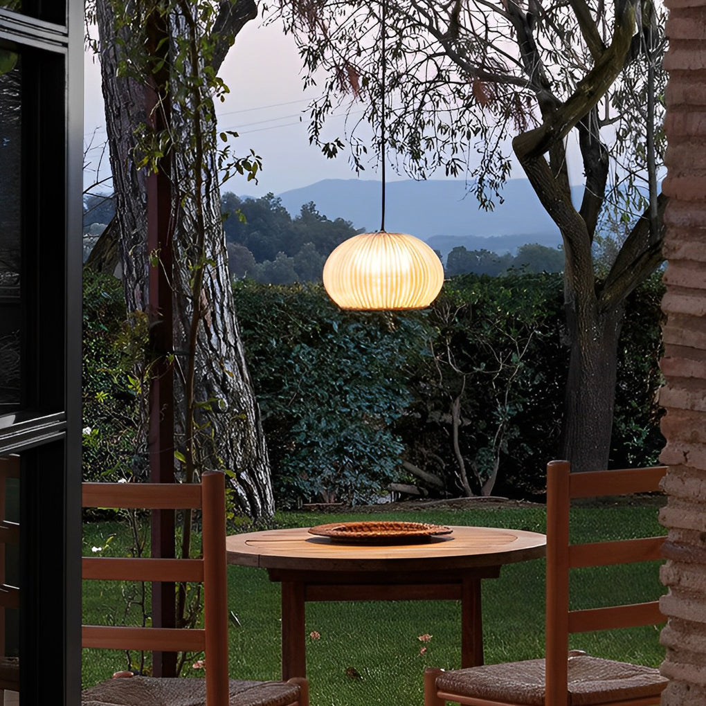 Rattan outdoor pendant light providing warm illumination near an outdoor wooden table.