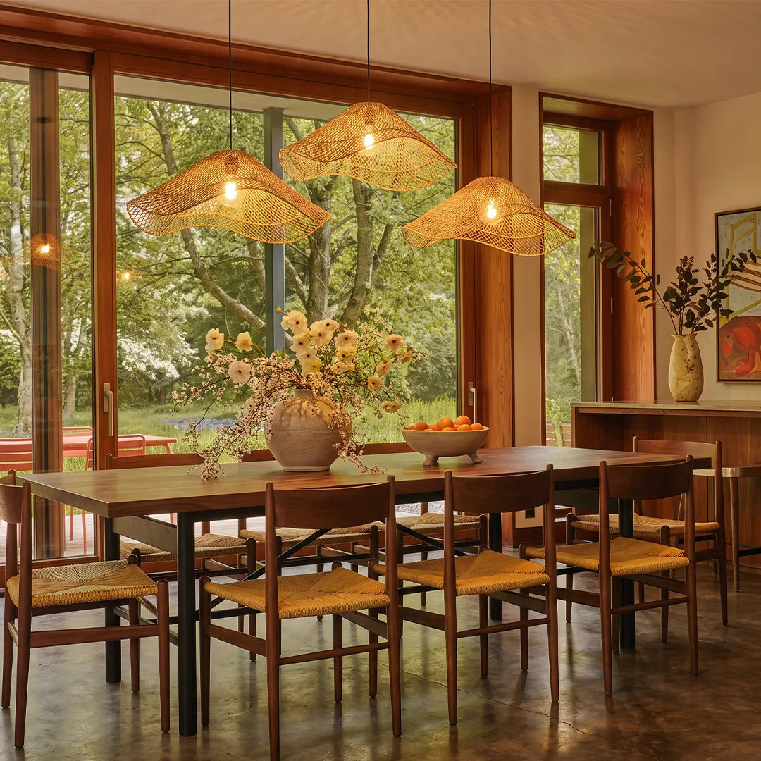 Rattan pendant light fixtures suspended above a dining table in a warm dining room with large windows.