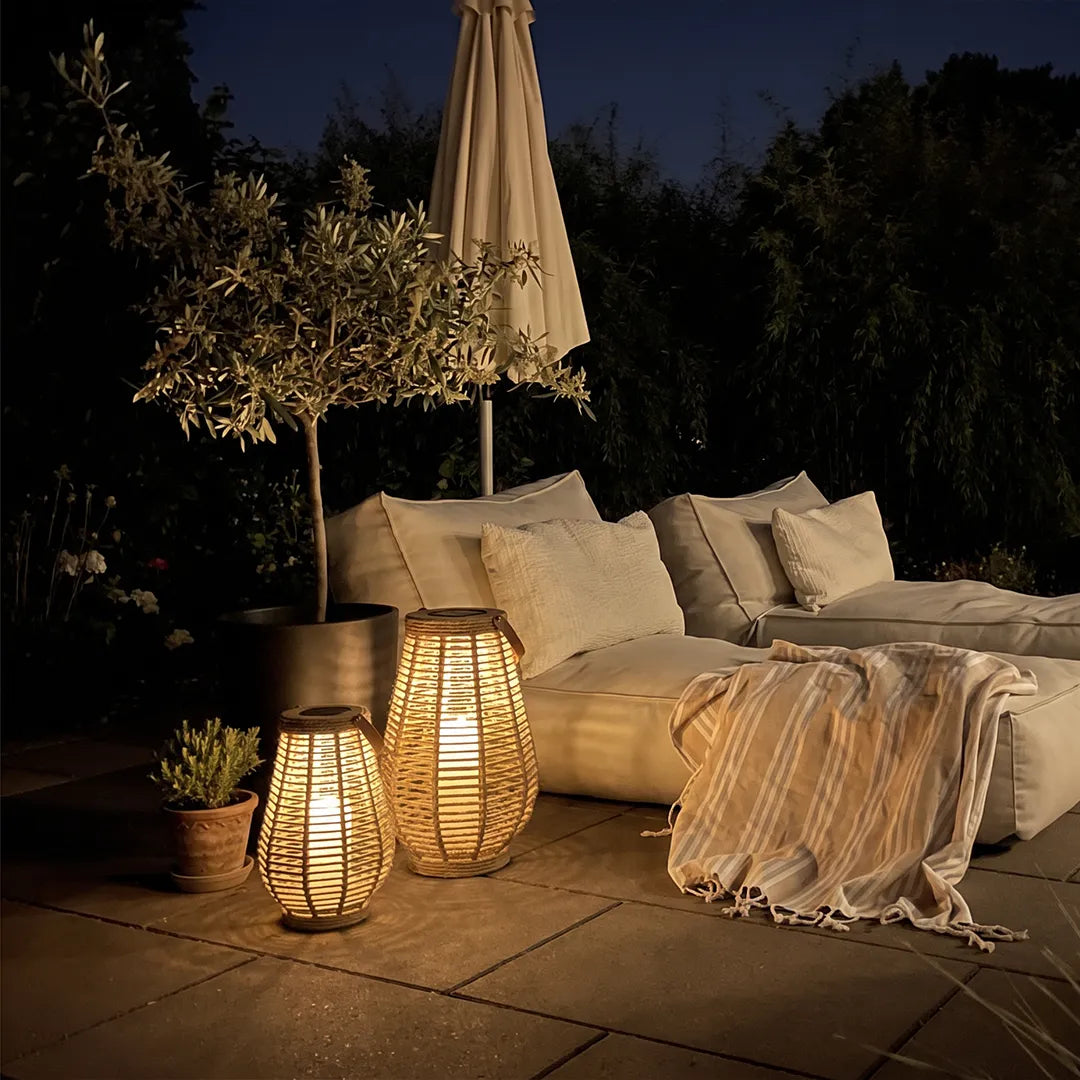 Rattan solar lanterns glowing beside cushioned outdoor lounge seating on a patio at night.