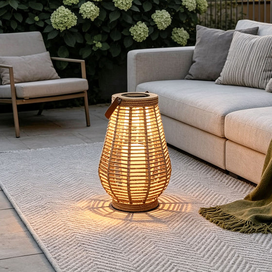 Rattan solar lantern glowing on a patio rug beside outdoor sofa seating and hydrangea plants.