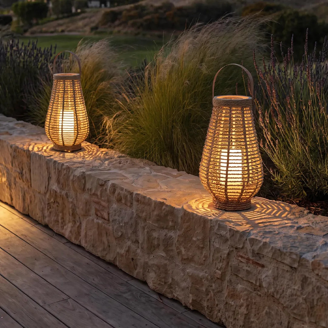 Rattan solar lanterns placed on a stone wall, casting warm light across a landscaped patio.