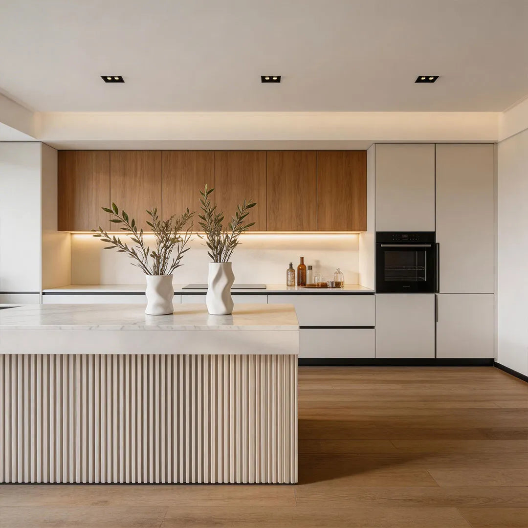 Recessed ceiling spot lights installed in a minimalist kitchen with a white island and warm wood cabinets.
