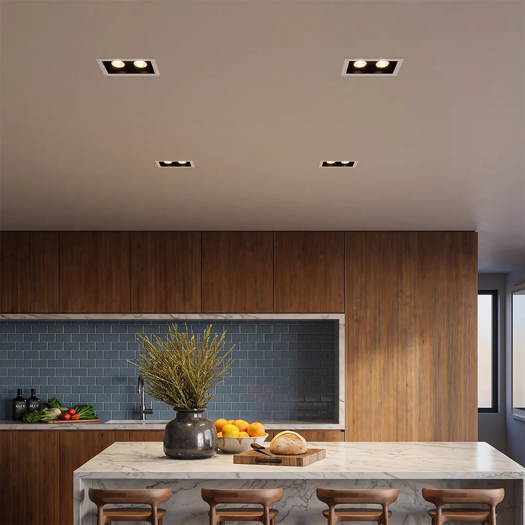 Recessed ceiling spot lights installed above a modern kitchen island with wood cabinetry and a tiled backsplash.