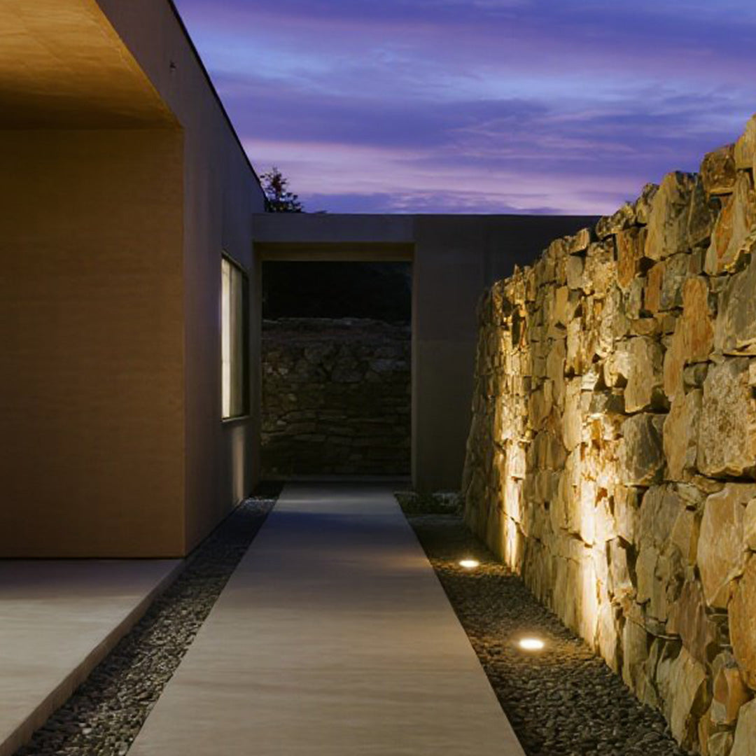 Recessed ground lighting highlighting modern concrete walkway and natural stone wall architecture