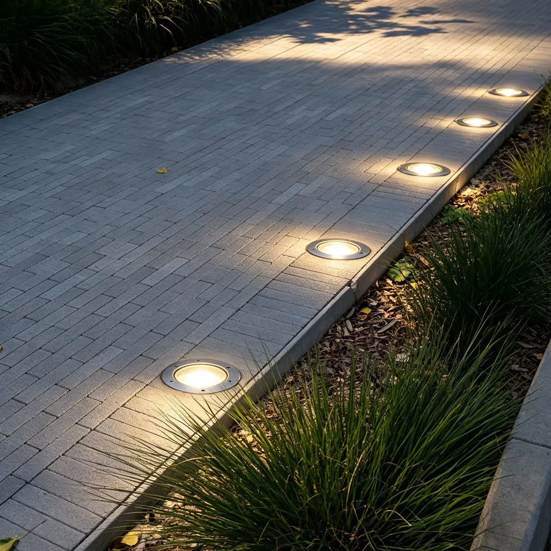 Recessed floor lighting lined along a paved garden walkway to provide soft illumination for modern landscape design.