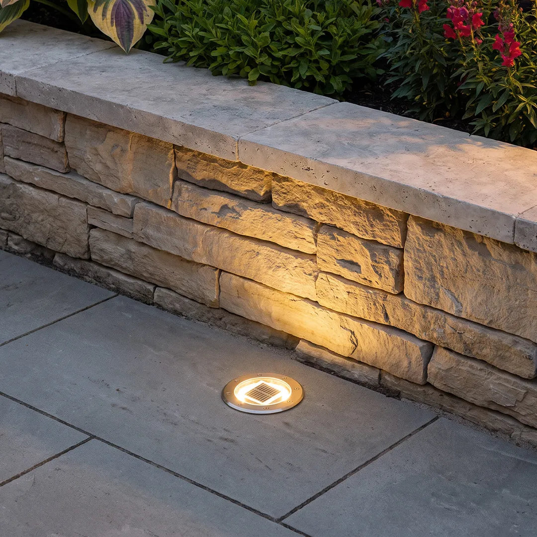 Recessed floor lighting installed beside a stone retaining wall to cast warm accent light onto the textured surface.