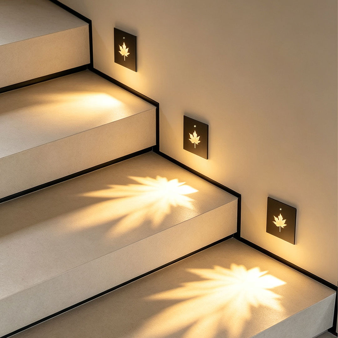 Recessed step lights casting decorative leaf-shaped illumination on modern staircase steps and walls.