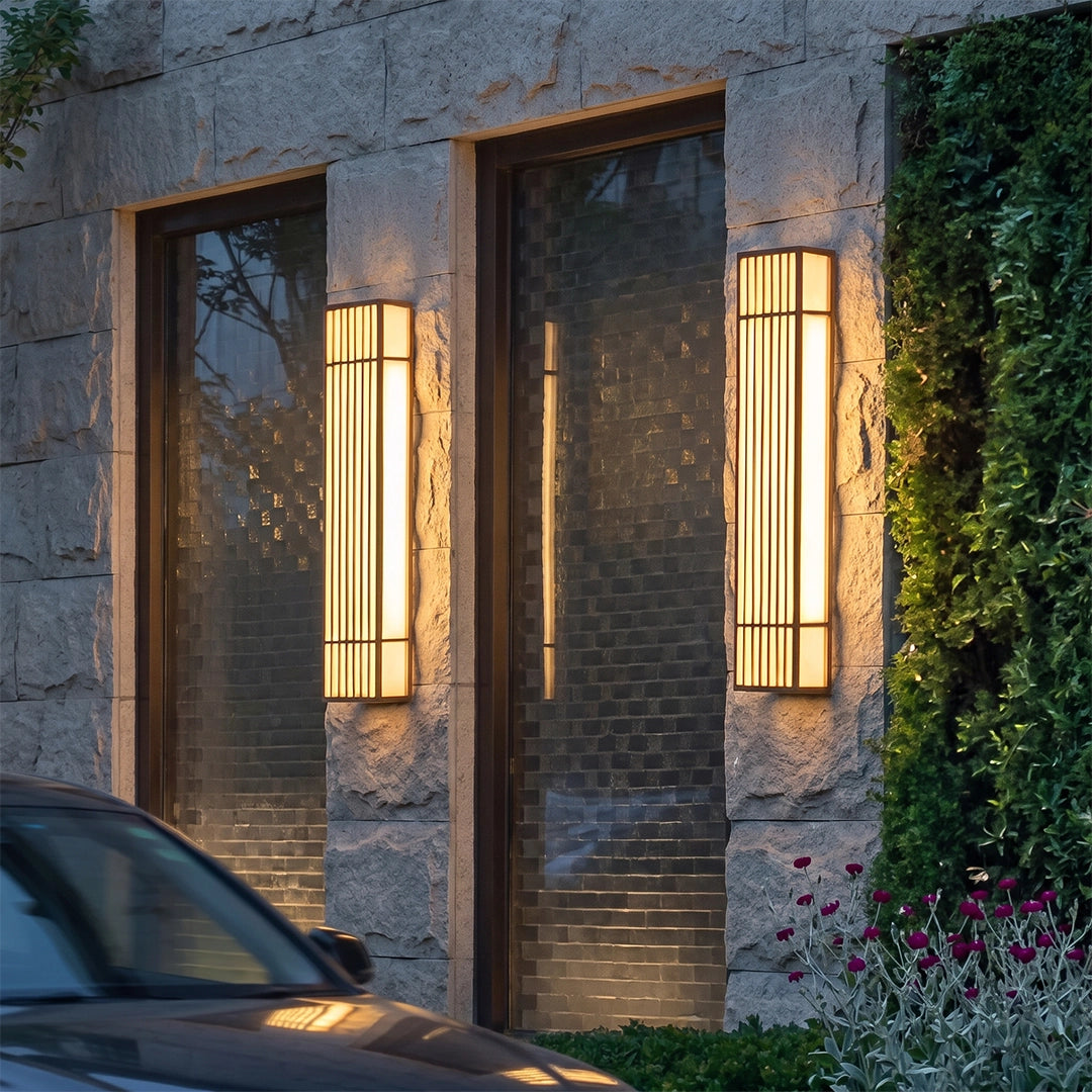 Rectangle LED outdoor wall light mounted on a stone wall beside a window, glowing warmly at dusk.